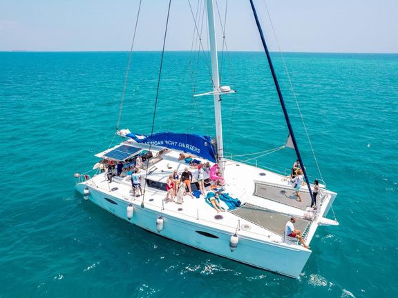 Guests on the deck of a white catamaran on turquoise water