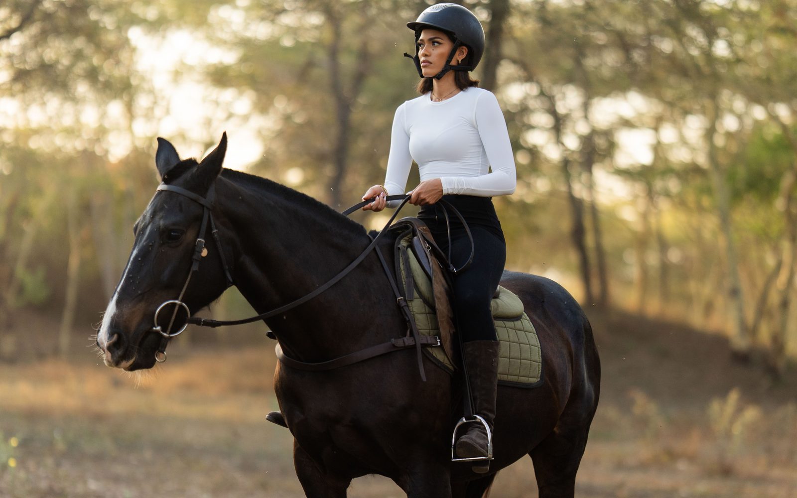 A Barafu Luxe guest riding a dark horse through acacia woodland at golden hour