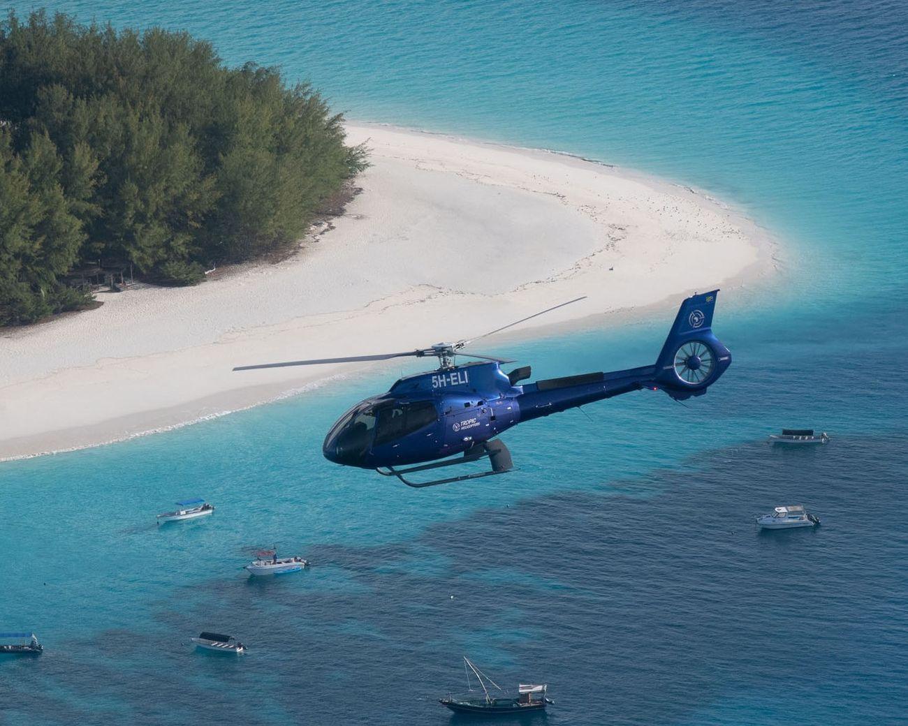 A blue helicopter over turquoise water beside a white sandbank off Zanzibar
